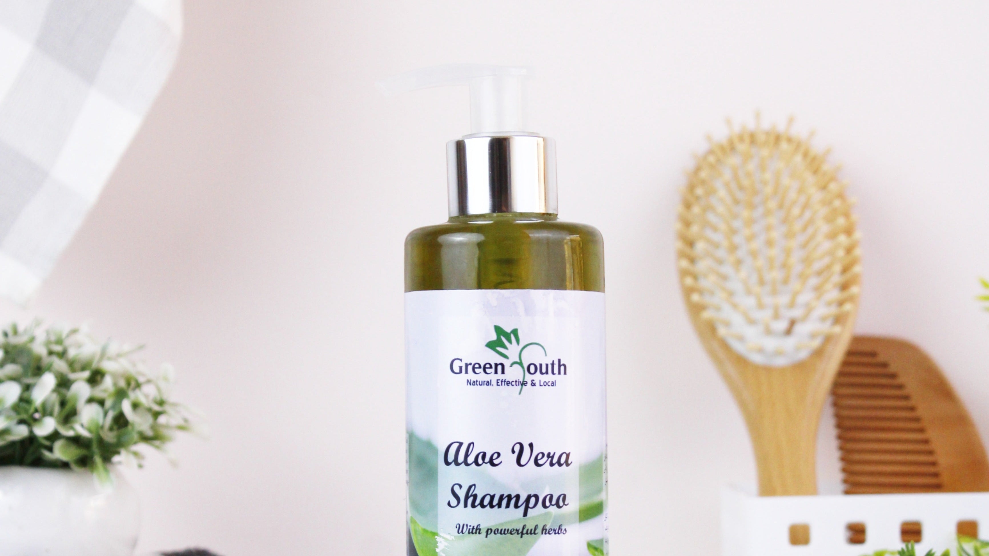 A bottle of Green South Aloe Vera Shampoo on a white surface with a blurred background